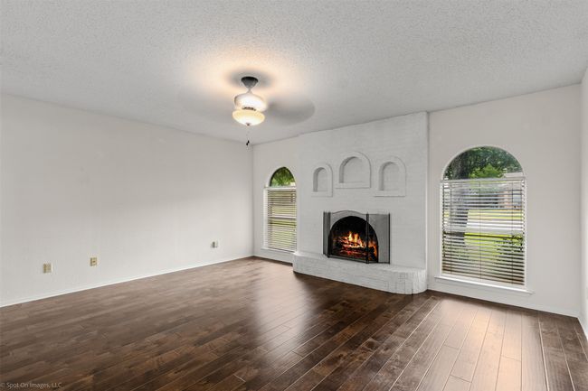 Unfurnished living room featuring a fireplace, plenty of natural light, dark wood-style flooring, a textured ceiling, and ceiling fan | Image 7