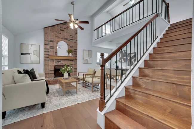 Living area featuring ceiling fan, wood finished floors, stairway, a fireplace, and high vaulted ceiling | Image 14