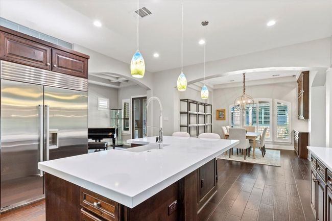 Kitchen featuring stainless steel built in refrigerator, arched walkways, dark wood-style flooring, visible vents, and light countertops | Image 13