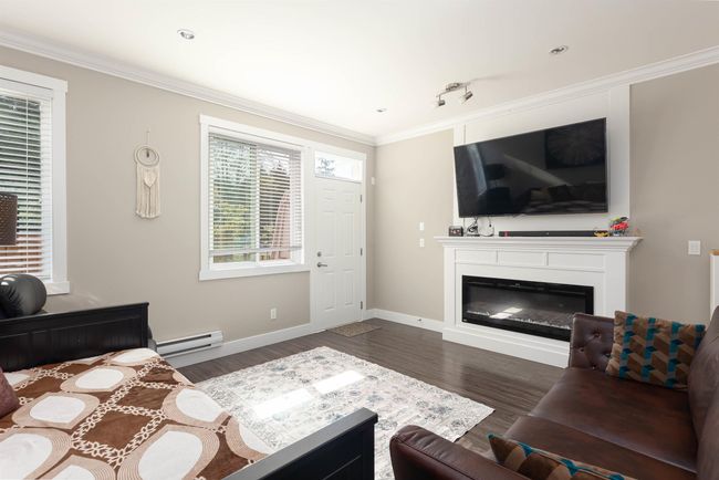 Living room featuring a baseboard radiator, a glass covered fireplace, wood finished floors, ornamental molding, and baseboards | Image 12