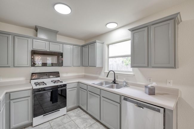 Kitchen featuring black microwave, white gas stove, dishwasher, gray cabinetry, and light countertops | Image 13
