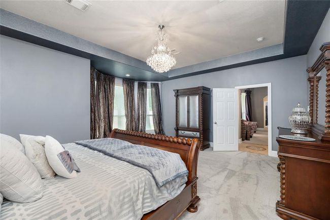 The oversized primary suite is a true retreat, featuring a spacious sitting area, elegant tray ceiling with detailed finishes, and plush carpeting throughout. Abundant natural light enhances the serene atmosphere, with direct access to a luxurious en-suite bathroom. | Image 15