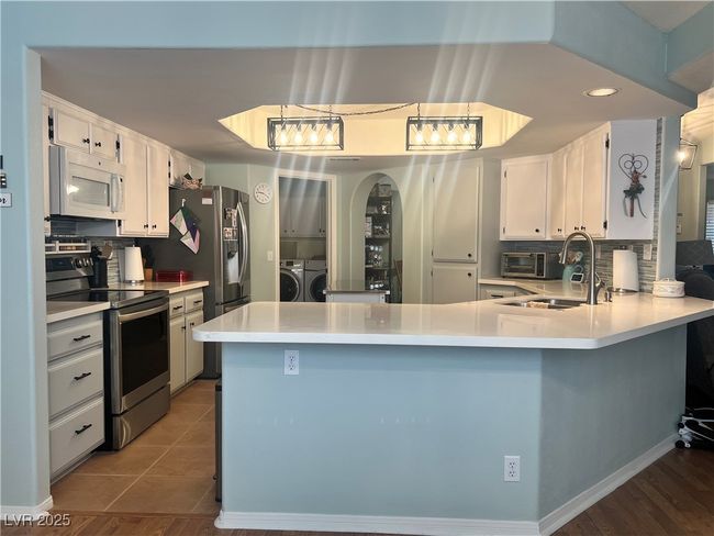 Kitchen with white microwave, stainless steel electric range, washing machine and dryer, a peninsula, and white cabinetry | Image 19