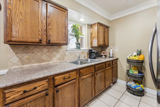 Kitchen featuring ornamental molding, backsplash, a sink, light tile patterned flooring, and brown cabinetry | Image 7