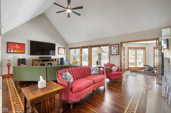 living area with a fireplace, a ceiling fan, wood finished floors, and high vaulted ceiling | Image 10
