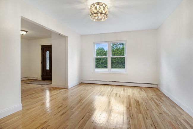Empty room with a baseboard radiator, hardwood / wood-style flooring, a chandelier, and baseboards | Image 5