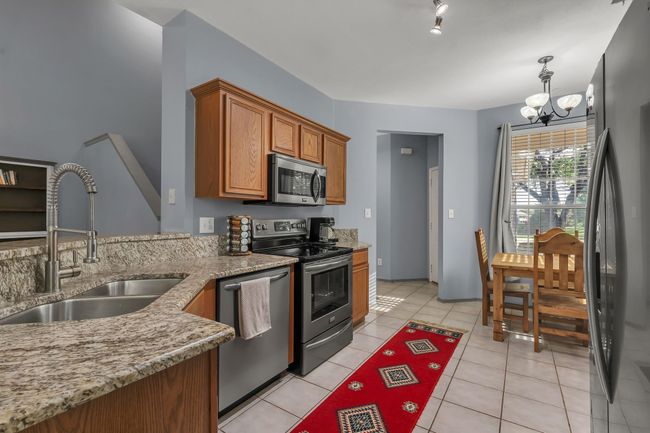 Kitchen with appliances with stainless steel finishes, brown cabinetry, a chandelier, light stone counters, and light tile patterned flooring | Image 10