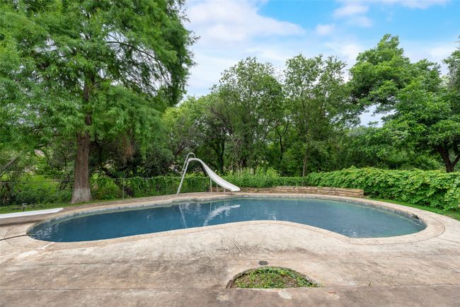 View of swimming pool with a water slide, a diving board, a patio, and view of wooded area | Image 33