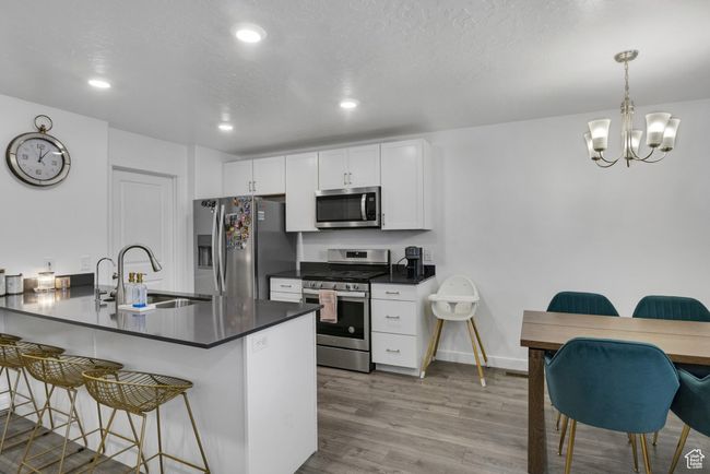Kitchen featuring stainless steel appliances, a sink, a breakfast bar area, dark countertops, and white cabinets | Image 7