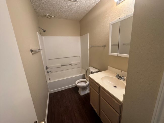 Full bath featuring a textured ceiling, vanity, wood finished floors, toilet, and shower / tub combination | Image 5