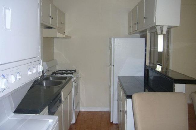Kitchen with under cabinet range hood, white appliances, dark wood-type flooring, and white cabinetry | Image 4
