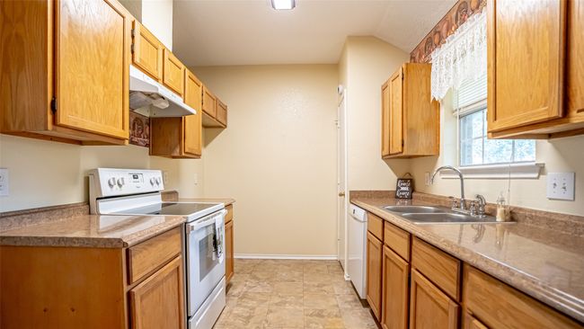 Kitchen with white appliances, under cabinet range hood, a sink, and light countertops | Image 7
