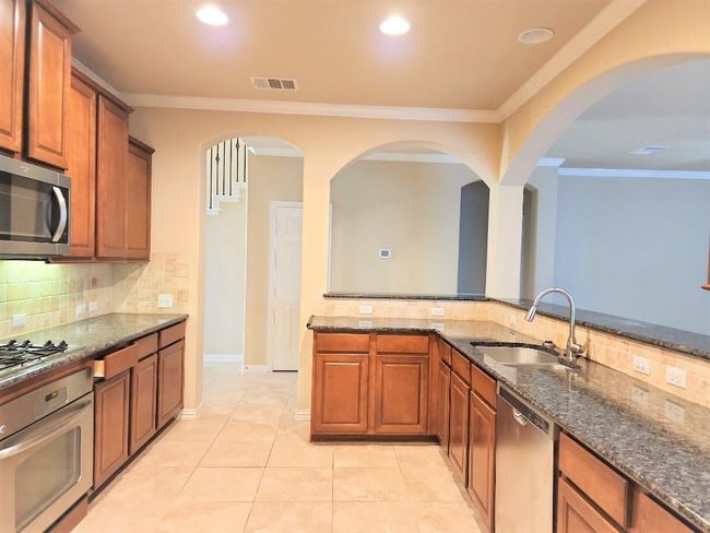 Kitchen with stainless steel appliances, a sink, backsplash, dark stone countertops, and crown molding | Image 7