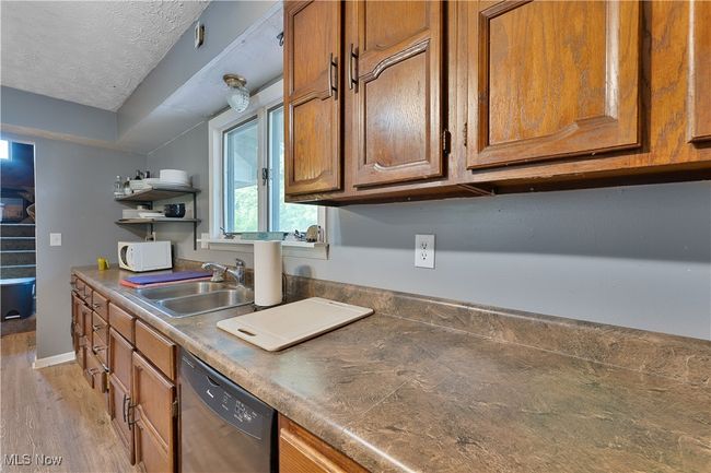 Kitchen featuring white microwave, dishwashing machine, brown cabinetry, light wood-style flooring, and open shelves | Image 8