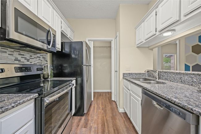 Kitchen featuring appliances with stainless steel finishes, a sink, white cabinetry, wood finished floors, and a textured ceiling | Image 10