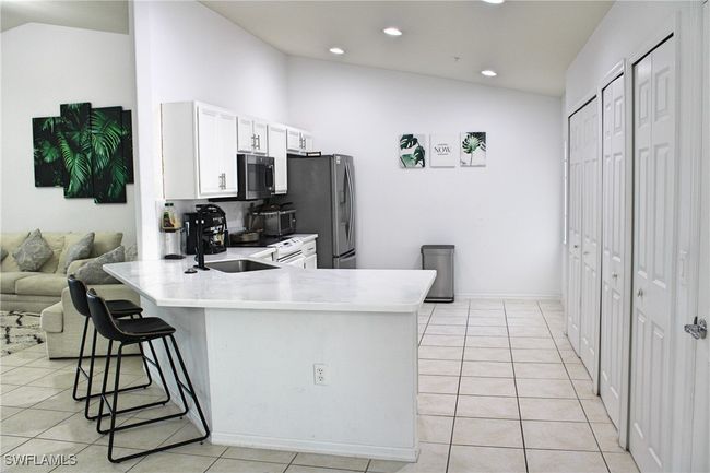 Kitchen featuring light tile patterned floors, vaulted ceiling, appliances with stainless steel finishes, and a kitchen breakfast bar | Image 4