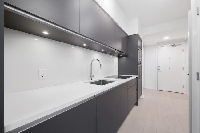 Kitchen with stainless steel microwave, black electric stovetop, recessed lighting, light countertops, and a sink | Image 7