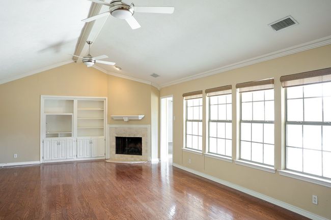 Unfurnished living room with a ceiling fan, wood finished floors, a fireplace, lofted ceiling, and crown molding | Image 4