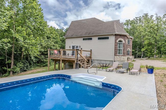 Swimming pool with a deck, stairs, a patio, and view of scattered trees | Image 56