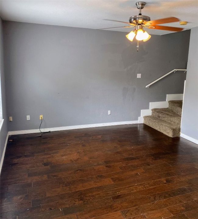 Unfurnished living room with baseboards, ceiling fan, dark wood finished floors, and stairs | Image 12