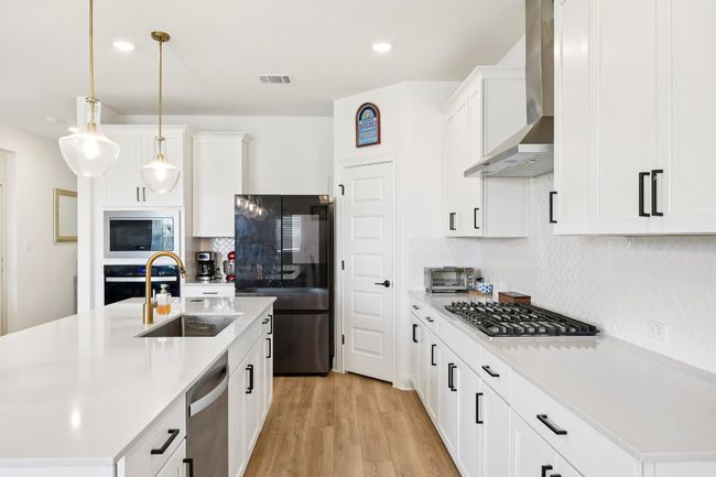 Kitchen featuring wall chimney exhaust hood, stainless steel appliances, light countertops, light wood-type flooring, and backsplash | Image 9