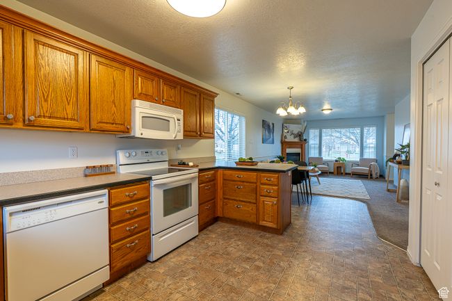 Kitchen featuring open floor plan, white appliances, a peninsula, a notable chandelier, and brown cabinetry | Image 11