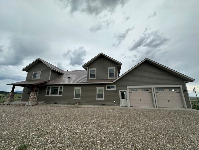 View of front of house with an attached garage, a porch, a metal roof, and gravel driveway | Image 36