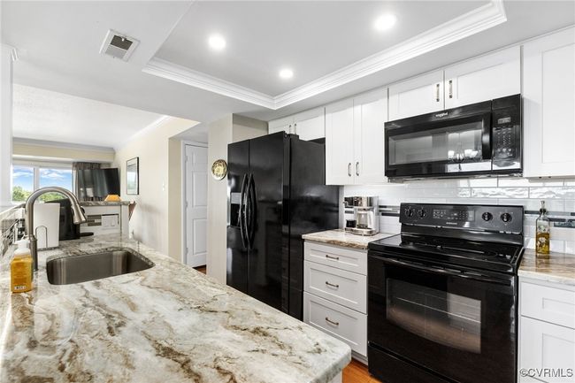 Kitchen with black appliances, backsplash, ornamental molding, a sink, and visible vents | Image 9