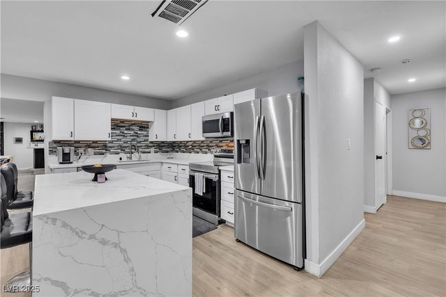 Kitchen with white cabinetry, a sink, stainless steel appliances, light stone countertops, and backsplash | Image 9