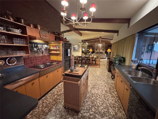 Kitchen with black appliances, a chandelier, a sink, decorative backsplash, and dark countertops | Image 25