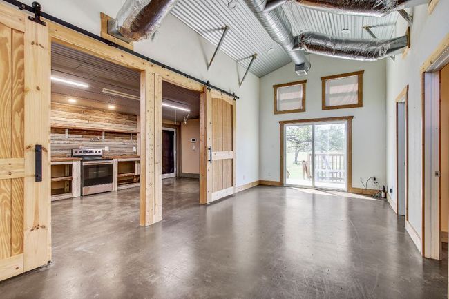 Unfurnished living room featuring baseboards, a high ceiling, a barn door, and concrete flooring | Image 26