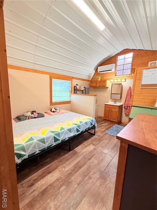 Bedroom with vaulted ceiling, a wall unit AC, light wood finished floors, and a sink | Image 14