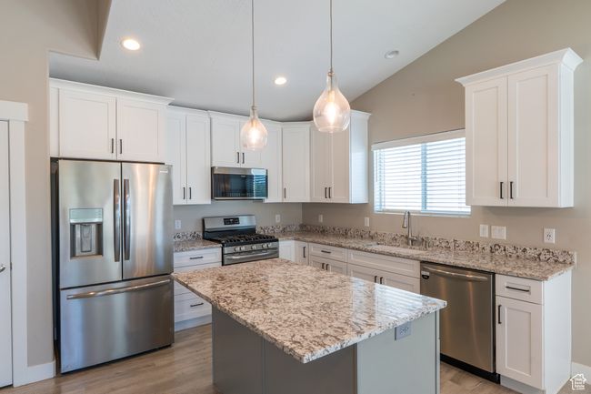 Kitchen featuring appliances with stainless steel finishes, white cabinets, lofted ceiling, a center island, and light stone countertops | Image 4