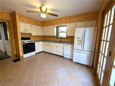 Kitchen featuring white cabinets, ceiling fan, light tile patterned floors, sink, and white appliances | Image 3