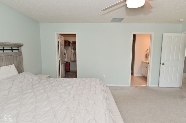 bedroom featuring a spacious closet, carpet floors, a textured ceiling, ensuite bathroom, and ceiling fan | Image 40