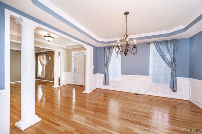 Unfurnished dining area with ornate columns, a chandelier, light wood-type flooring, crown molding, and a wainscoted wall | Image 10
