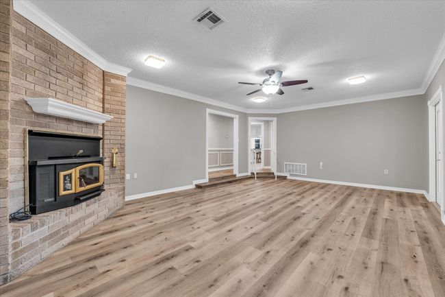 Unfurnished living room with a brick fireplace, light wood-style floors, a ceiling fan, a textured ceiling, and crown molding | Image 12