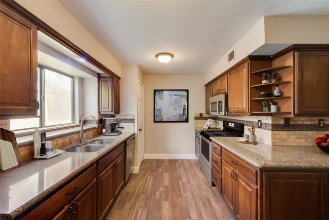 Kitchen featuring stainless steel appliances, open shelves, backsplash, light stone counters, and light wood-style floors | Image 5