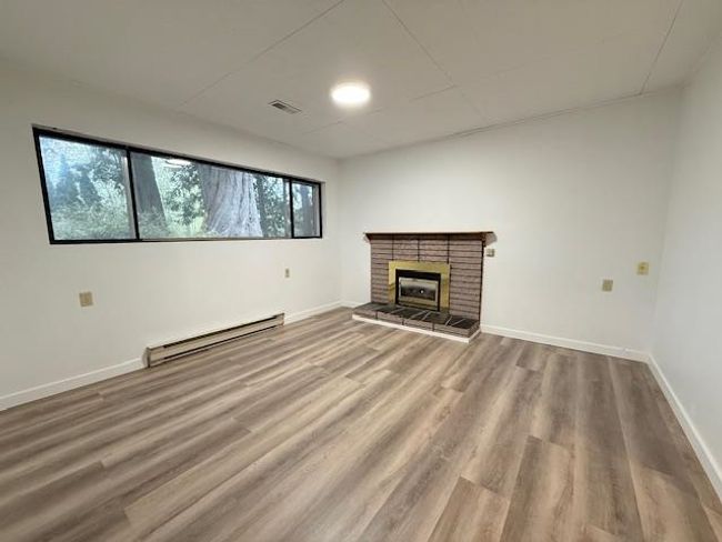 Unfurnished living room featuring a baseboard radiator, wood finished floors, baseboards, and a fireplace | Image 17