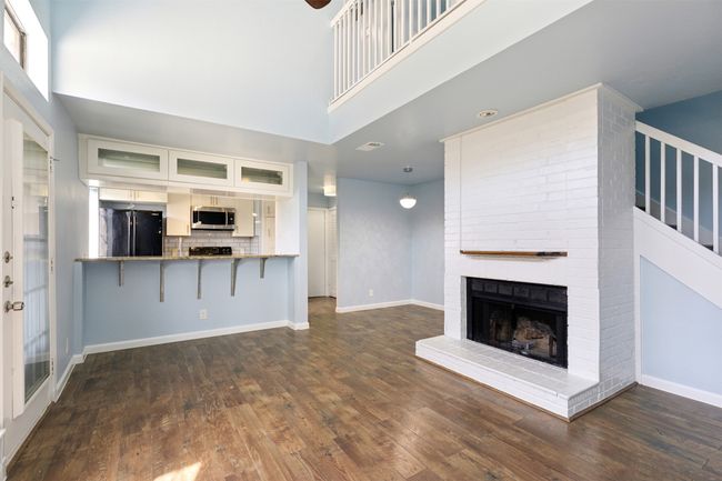 Unfurnished living room with wood-style flooring, a fireplace, a towering ceiling, and baseboards | Image 4