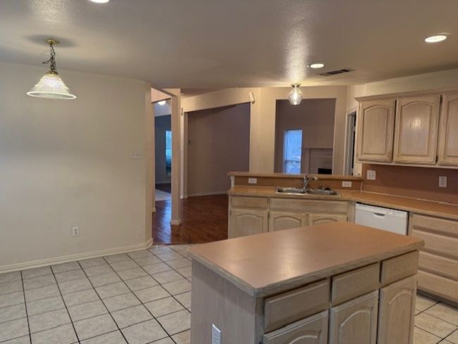 Kitchen with light tile patterned floors, recessed lighting, a kitchen island, dishwasher, and decorative light fixtures | Image 9