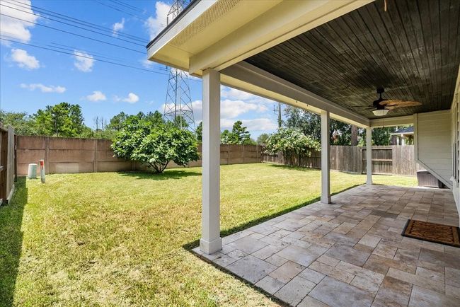 A spacious backyard with a covered patio featuring a tiled floor and ceiling fan. The yard is fenced with lush lawn space, ideal for outdoor activities or relaxation. With NO back neighbors | Image 42