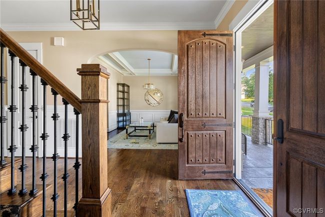 Entryway featuring arched walkways, crown molding, dark wood-style flooring, a wainscoted wall, and stairway | Image 4