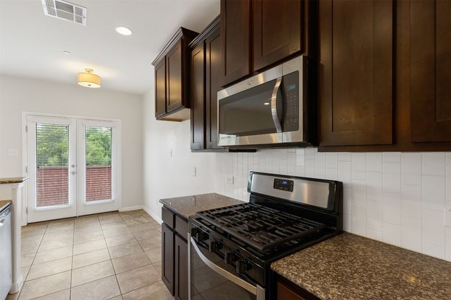Kitchen featuring stainless steel appliances, dark brown cabinetry, decorative backsplash, french doors, and dark stone counters | Image 12