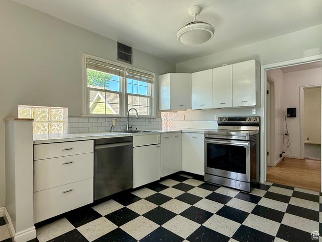 Kitchen with stainless steel appliances, dark flooring, light countertops, a sink, and white cabinets | Image 14