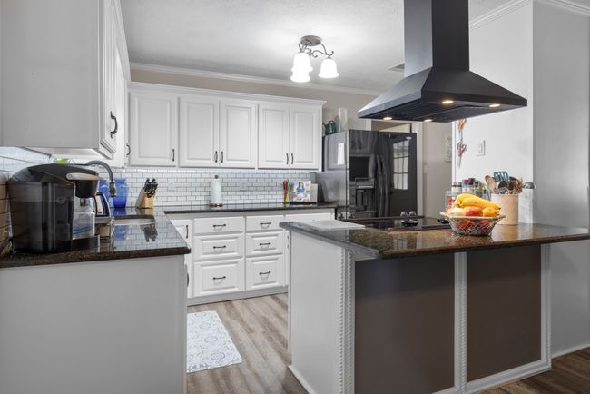 Kitchen with island range hood, black refrigerator with ice dispenser, light wood-type flooring, ornamental molding, and white cabinets | Image 5