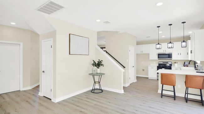 Kitchen featuring a kitchen breakfast bar, light wood-type flooring, stainless steel appliances, white cabinets, and visible vents | Image 6