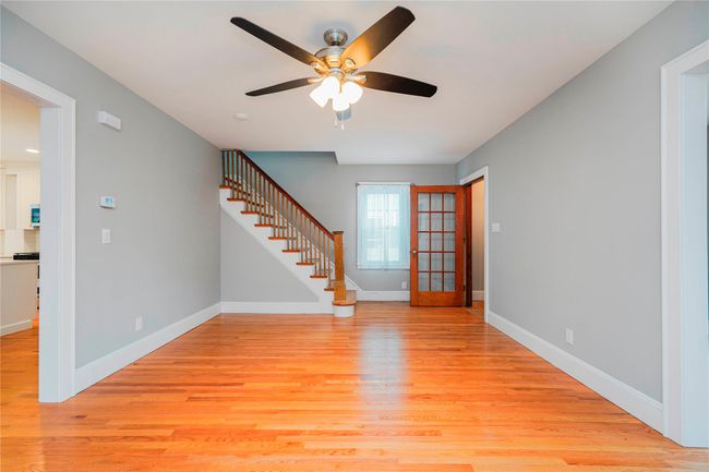 Unfurnished living room with stairs, light wood-style flooring, baseboards, and ceiling fan | Image 8