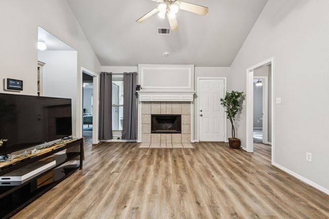 Unfurnished living room with lofted ceiling, ceiling fan, wood finished floors, and a fireplace | Image 11