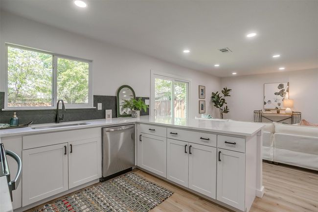 Kitchen featuring stainless steel dishwasher, a peninsula, light wood finished floors, backsplash, and light countertops | Image 12